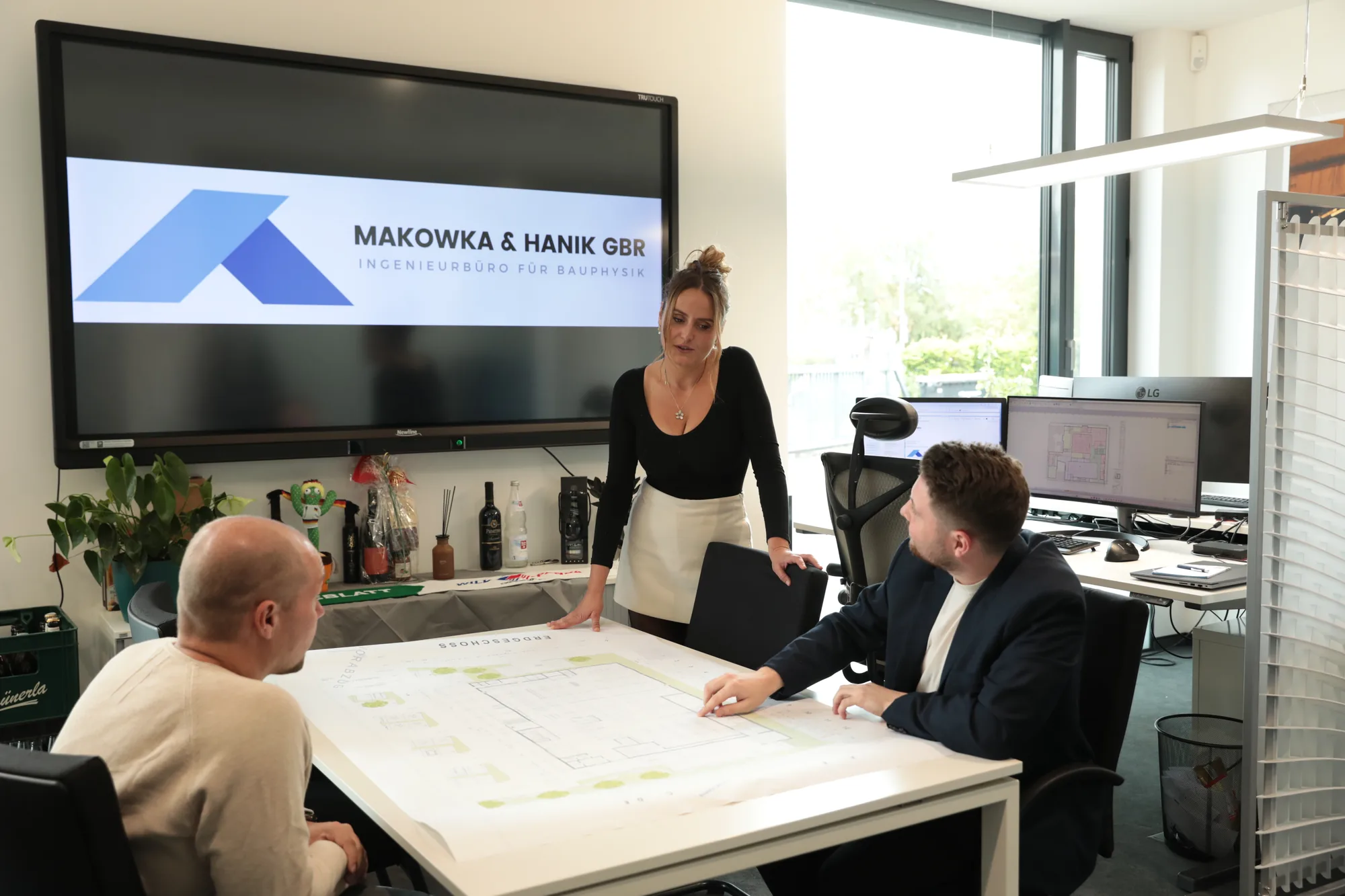 ibmh-karriere-zusammenarbeit-01-desktop - Ingenieurbüro Makowka & Hanik Drei Kolleginnen und Kollegen besprechen einen ausgedruckten Bauplan am Plantisch